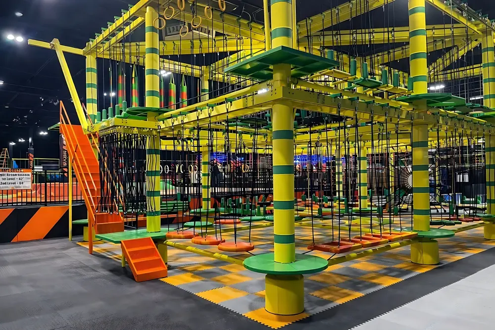Indoor ropes course with yellow and green towers, rope bridges and swinging platforms